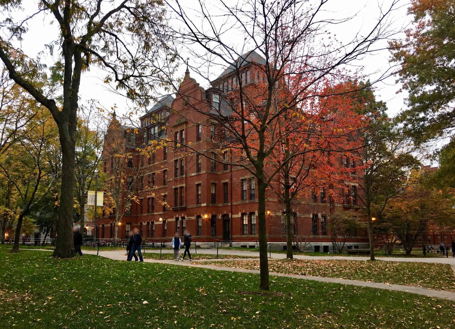 Red-brick campus building framed by autumn trees; faces blurred
