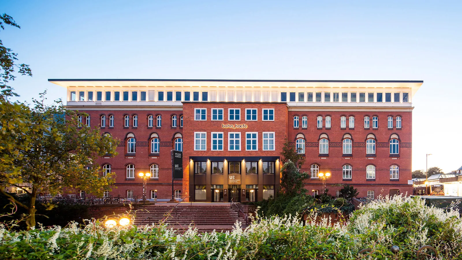 Red-brick university building with a central entrance and landscaped garden